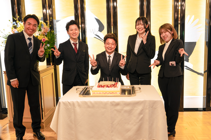大きなケーキを前にして記念写真を撮る北澤副社長と新入社員