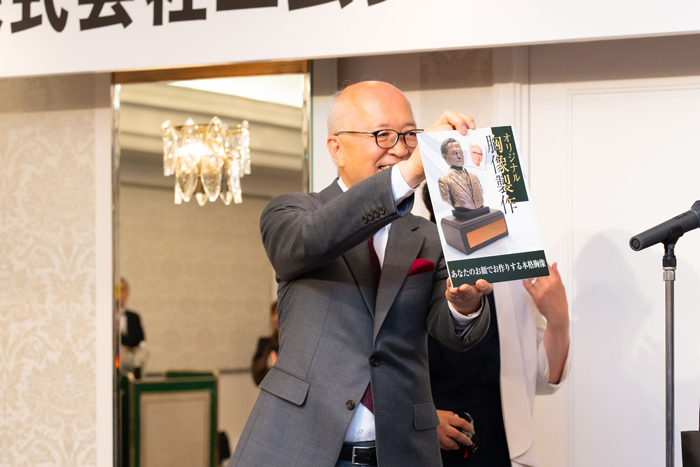 プレゼントされた銅像のサンプルを見せる社長